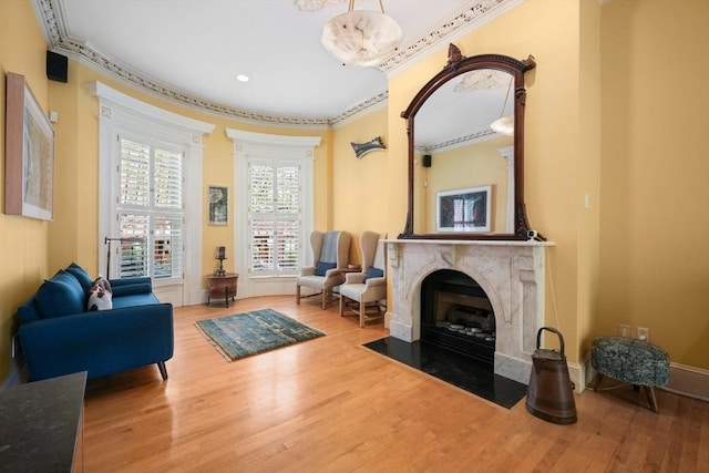 living area with baseboards, ornamental molding, a high end fireplace, and wood finished floors