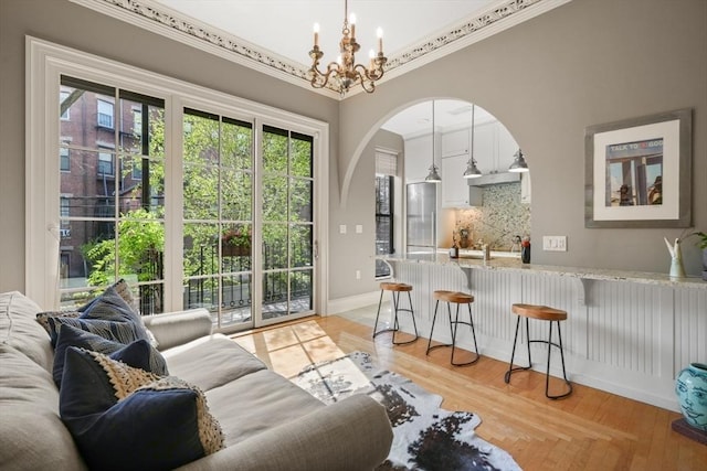 interior space featuring arched walkways, ornamental molding, an inviting chandelier, and light wood-style flooring