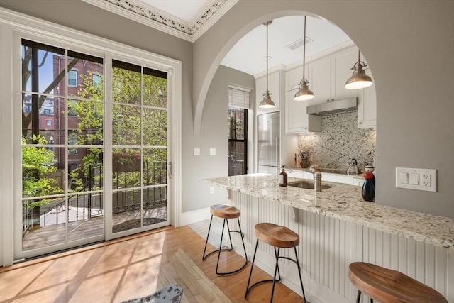 kitchen with under cabinet range hood, light wood finished floors, decorative backsplash, light stone countertops, and built in fridge