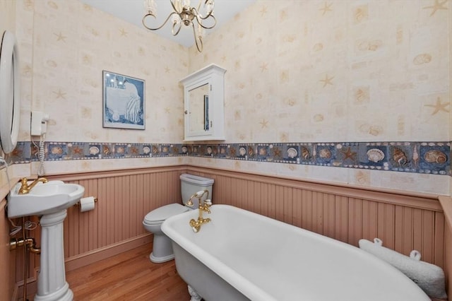 full bathroom with wallpapered walls, a freestanding tub, wood finished floors, and a wainscoted wall