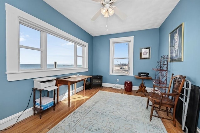 living area featuring wood finished floors, baseboards, and ceiling fan