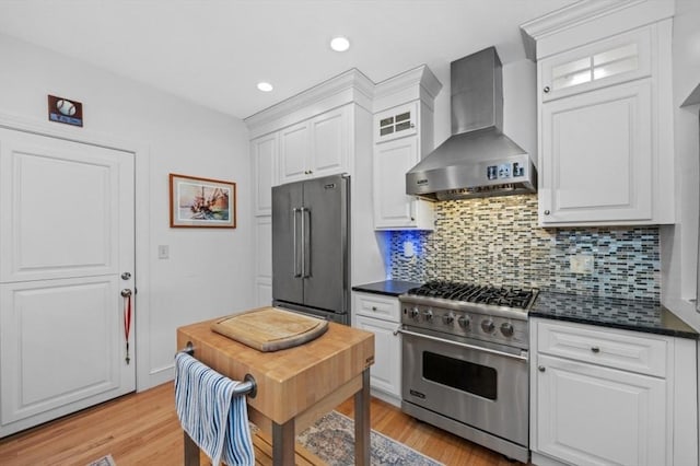 kitchen featuring white cabinets, dark countertops, wall chimney range hood, high quality appliances, and light wood-type flooring