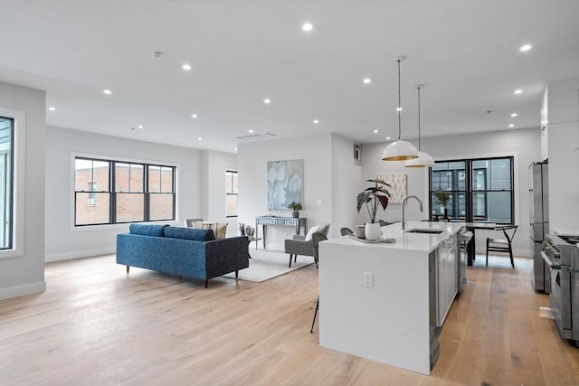 kitchen featuring pendant lighting, light hardwood / wood-style flooring, stainless steel appliances, sink, and a center island with sink