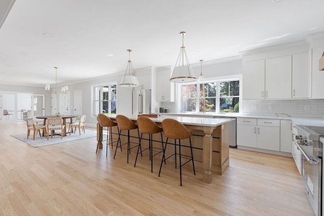 kitchen with white cabinetry, a kitchen island, stainless steel appliances, light hardwood / wood-style flooring, and decorative light fixtures