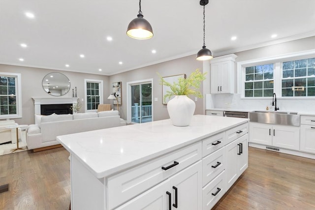kitchen with a sink, a center island, decorative light fixtures, light wood-style flooring, and crown molding