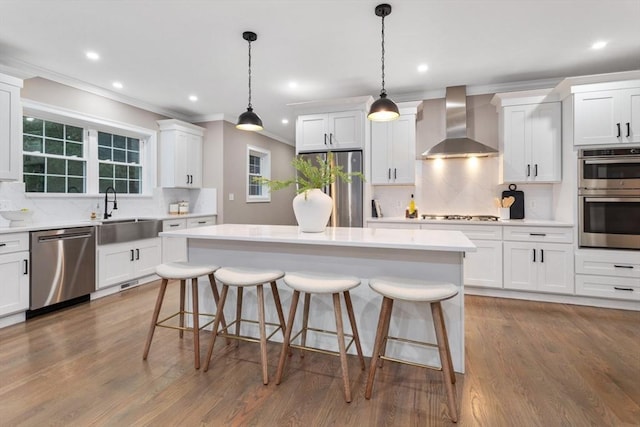 kitchen with wall chimney exhaust hood, stainless steel appliances, a sink, decorative backsplash, and a kitchen island