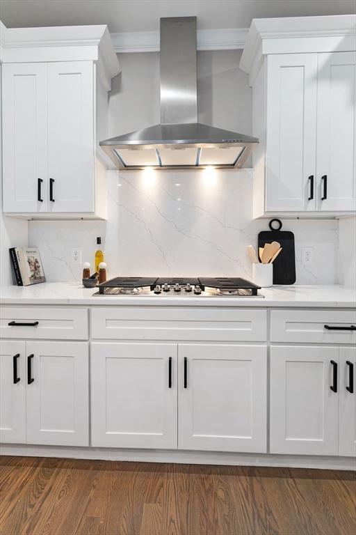kitchen with wall chimney exhaust hood, decorative backsplash, white cabinetry, dark wood finished floors, and stainless steel gas stovetop