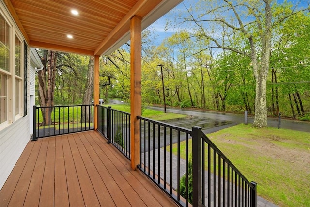 wooden deck with covered porch, a lawn, and view of scattered trees