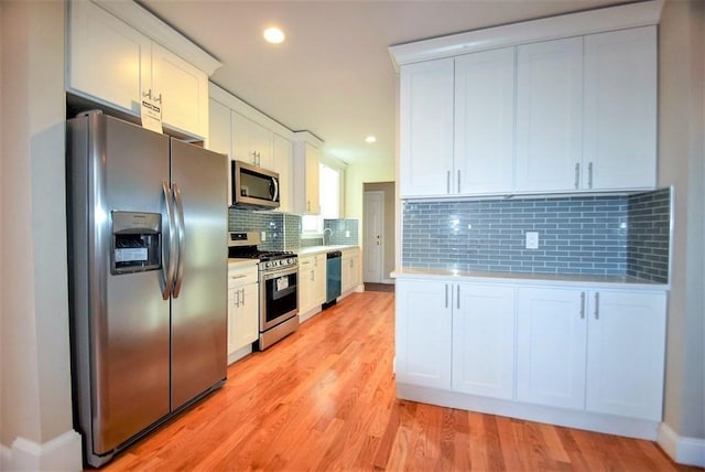 kitchen featuring tasteful backsplash, light wood-type flooring, appliances with stainless steel finishes, tile counters, and white cabinets