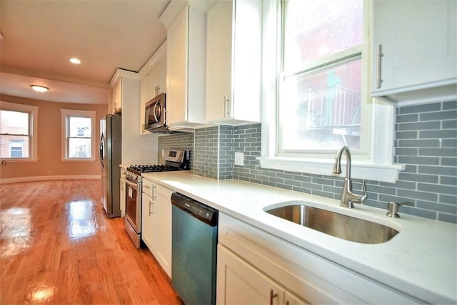 kitchen with sink, appliances with stainless steel finishes, tasteful backsplash, white cabinets, and light wood-type flooring