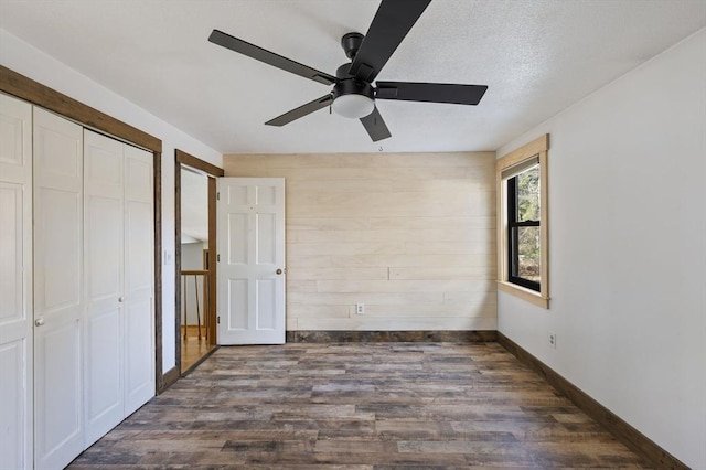 unfurnished bedroom featuring dark wood-type flooring, ceiling fan, and wooden walls