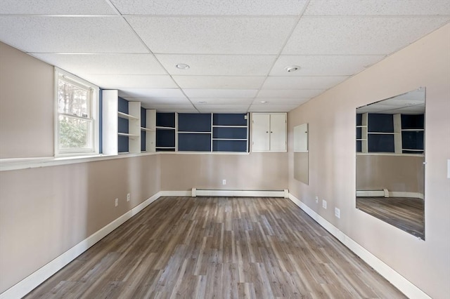 spare room featuring wood-type flooring, a drop ceiling, and baseboard heating