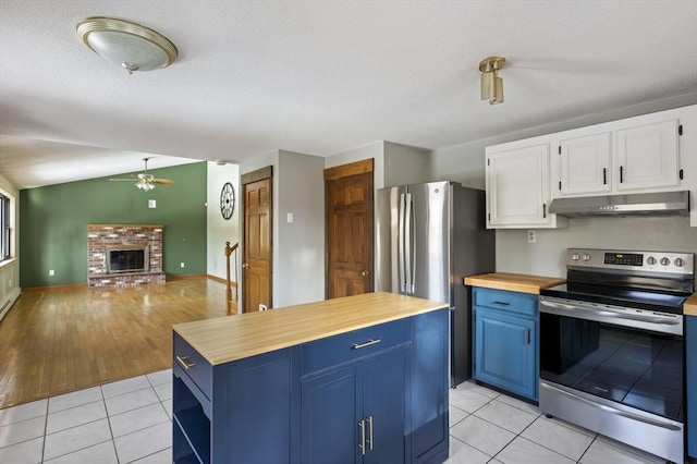 kitchen featuring light tile patterned floors, blue cabinetry, appliances with stainless steel finishes, white cabinetry, and a brick fireplace