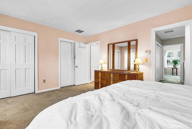 carpeted bedroom featuring baseboards, visible vents, and multiple closets