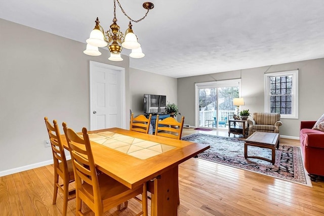 dining area featuring baseboards, light wood-type flooring, and a notable chandelier