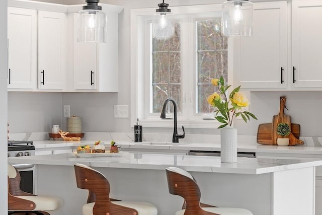 kitchen featuring white cabinetry, hanging light fixtures, a kitchen breakfast bar, and a sink