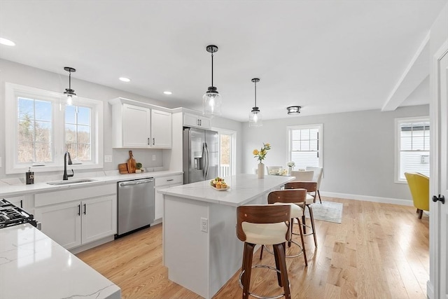 kitchen with a breakfast bar area, a sink, light wood-style floors, stainless steel appliances, and a kitchen island