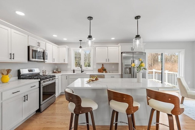 kitchen featuring a breakfast bar, a sink, a center island, appliances with stainless steel finishes, and white cabinetry