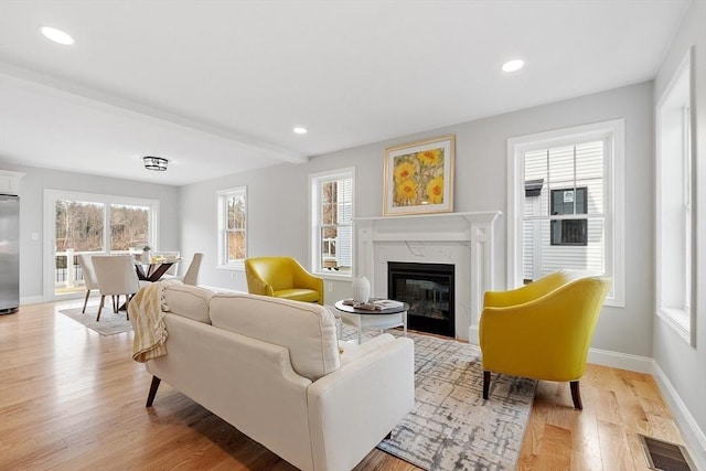 living room featuring light wood finished floors, a premium fireplace, baseboards, visible vents, and recessed lighting