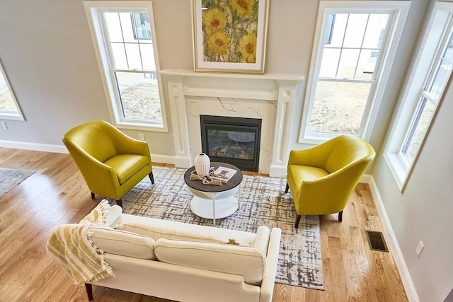 sitting room featuring a healthy amount of sunlight, visible vents, baseboards, wood finished floors, and a high end fireplace
