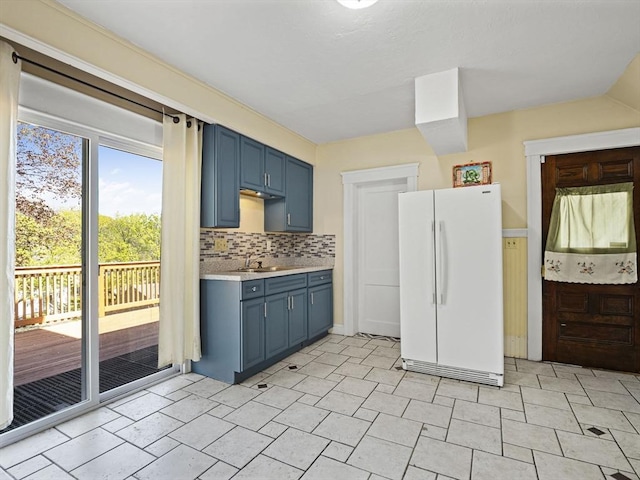 kitchen featuring decorative backsplash, blue cabinetry, light countertops, a sink, and freestanding refrigerator