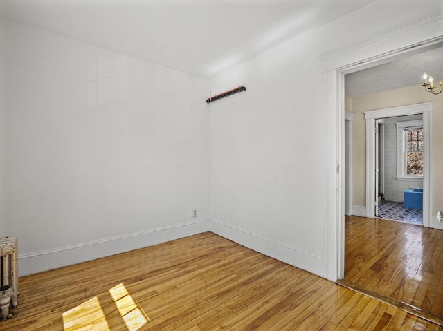 spare room featuring baseboards, an inviting chandelier, and light wood-type flooring