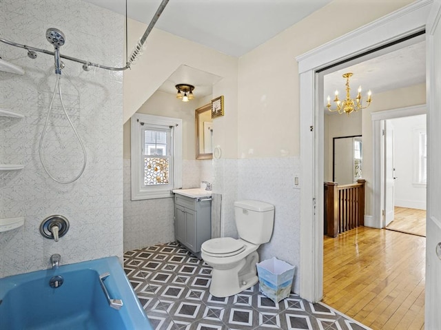 bathroom with an inviting chandelier, vanity, toilet, tile walls, and  shower combination