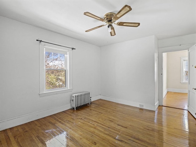 empty room with plenty of natural light, a ceiling fan, radiator, and hardwood / wood-style flooring