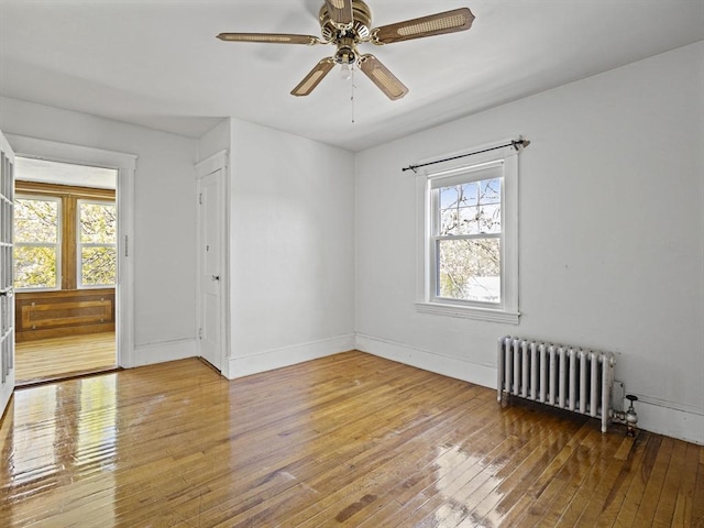 empty room with wood-type flooring, a ceiling fan, radiator, and a healthy amount of sunlight