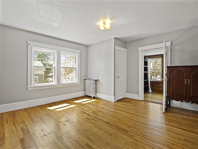 unfurnished bedroom featuring baseboards, light wood finished floors, radiator heating unit, and multiple windows