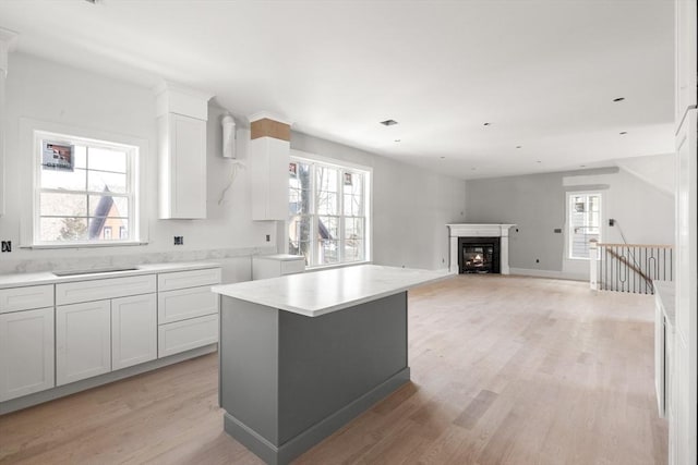 kitchen with a fireplace, light countertops, light wood-style flooring, white cabinets, and baseboards