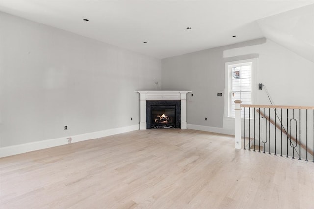 unfurnished living room with lofted ceiling, light wood-style flooring, baseboards, and a premium fireplace