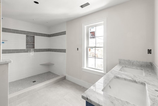 full bathroom with tiled shower, a sink, baseboards, and double vanity