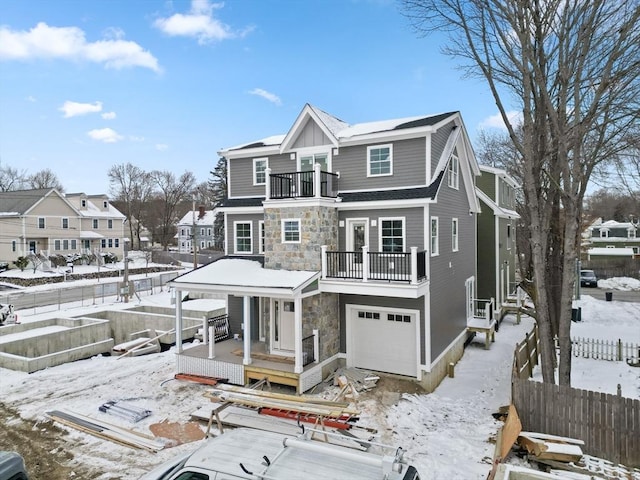 view of front of home featuring a garage, a balcony, stone siding, a residential view, and fence