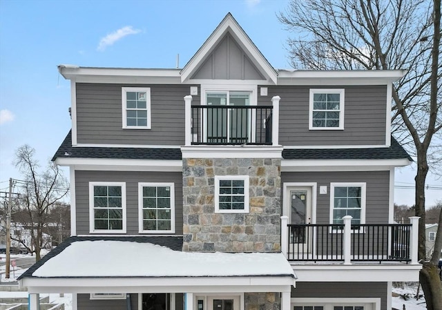 exterior space featuring board and batten siding, stone siding, roof with shingles, and a balcony