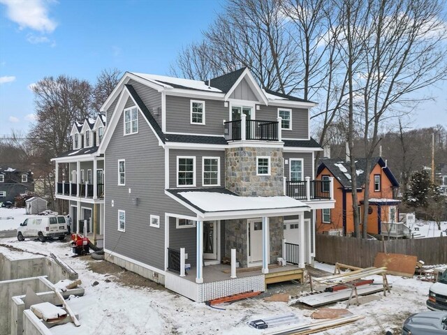 snow covered house with a balcony, stone siding, and fence