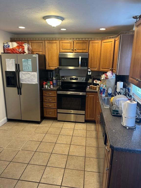 kitchen featuring brown cabinets, light tile patterned floors, dark countertops, recessed lighting, and appliances with stainless steel finishes