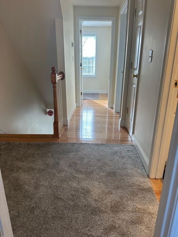 hall featuring light carpet, light wood-style flooring, baseboards, and an upstairs landing