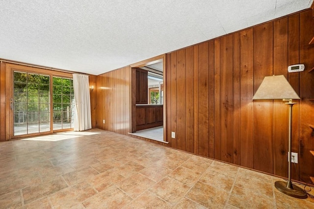 empty room with stone finish flooring, a textured ceiling, and wood walls