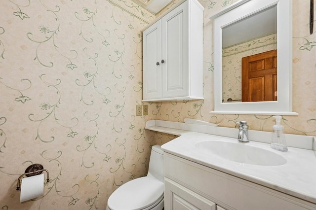 bathroom with vanity, toilet, and wallpapered walls