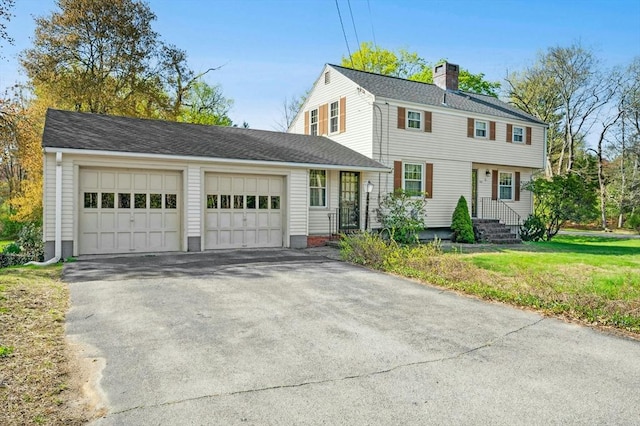 colonial inspired home featuring an attached garage, a shingled roof, driveway, and a chimney