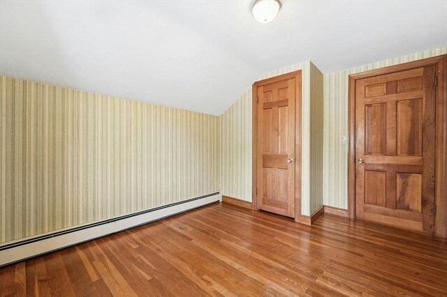 additional living space with wood finished floors, lofted ceiling, a baseboard heating unit, and wallpapered walls