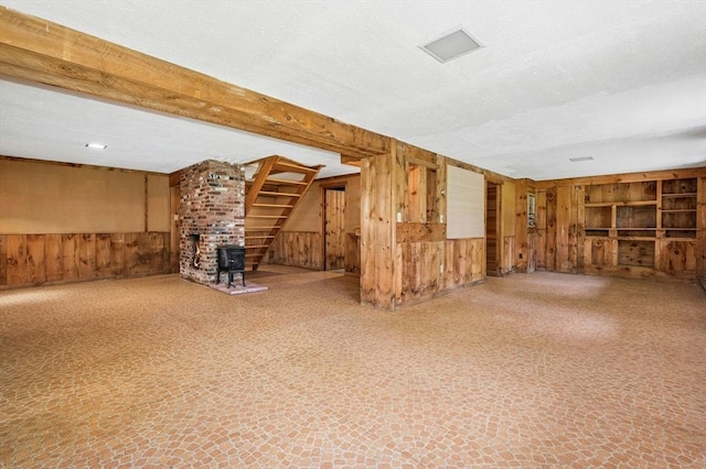 finished below grade area featuring wood walls, a textured ceiling, a wood stove, and stairway