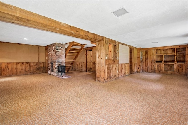 finished below grade area featuring wood walls, a textured ceiling, built in shelves, and a wood stove