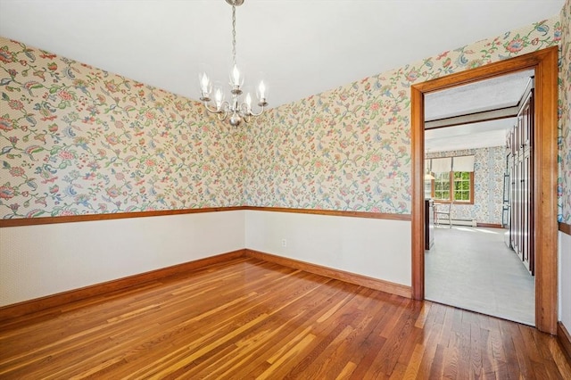 spare room with baseboards, wallpapered walls, a chandelier, hardwood / wood-style flooring, and a baseboard radiator
