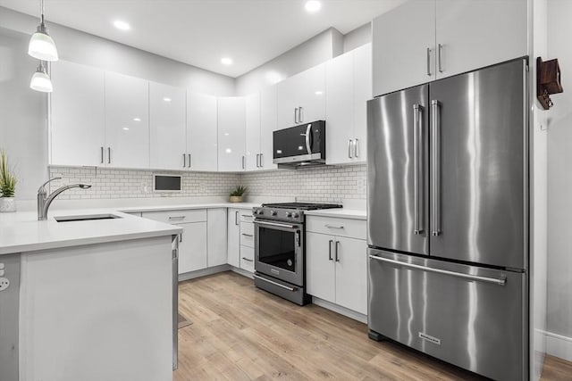 kitchen featuring sink, appliances with stainless steel finishes, white cabinetry, light hardwood / wood-style floors, and decorative light fixtures