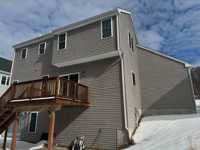 snow covered back of property with a wooden deck