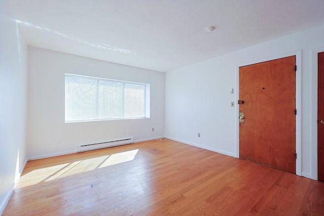 empty room featuring a baseboard radiator, baseboards, and light wood finished floors