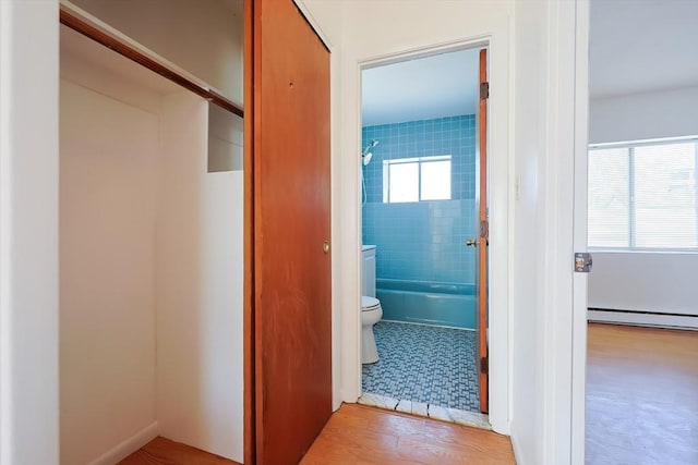 interior space with wood finished floors, toilet,  shower combination, and a baseboard radiator