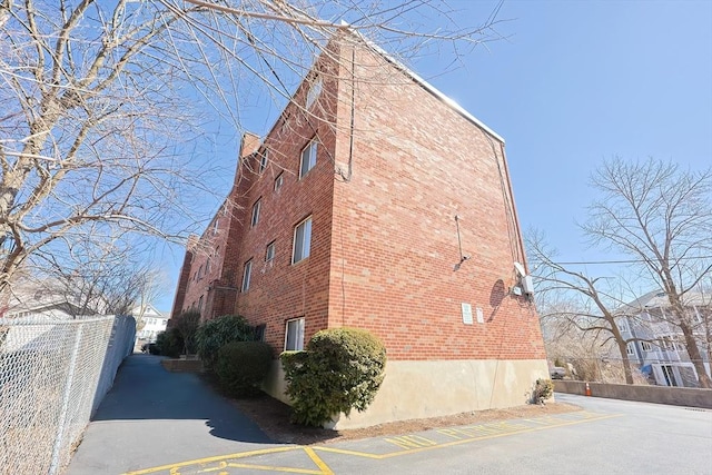 view of side of home featuring brick siding, uncovered parking, and fence